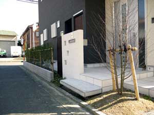 写真の時点ではまだ成長していないですが、塀に生垣で境界を仕切り、玄関横にシンボルツリーを植え、白い門塀が映える家まわり空間にしました。